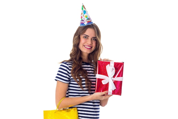 Jovem mulher bonita no boné de celebração com cabelo comprido, segurando o presente vermelho e olhando para ele