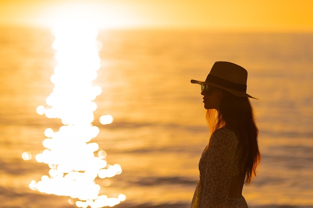 Jovem mulher bonita no chapéu de palha na praia ao pôr do sol