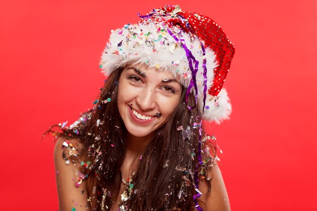 Jovem mulher bonita no sorriso do chapéu de Papai Noel. Conto de Natal. Cartão postal. Vertical. Vermelho.