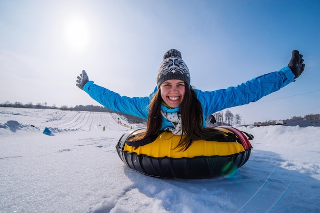 Jovem mulher bonita no tubo de neve levanta as mãos no slide da colina de neve
