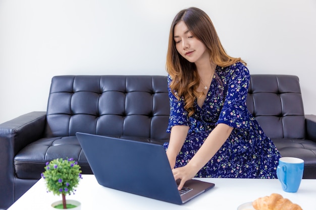 Jovem mulher bonita no vestido azul, trabalhando em seu computador em sua sala de estar em casa