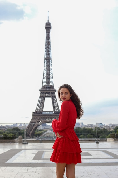 Jovem mulher bonita no vestido vermelho em pé na frente da torre eiffel em paris