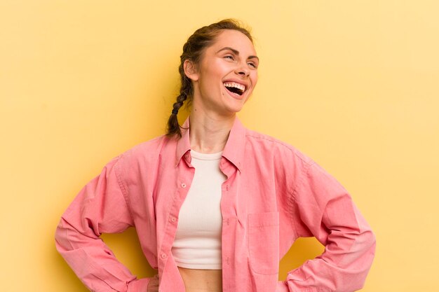 Jovem mulher bonita olhando feliz alegre e confiante sorrindo orgulhosamente e olhando para o lado com as duas mãos nos quadris