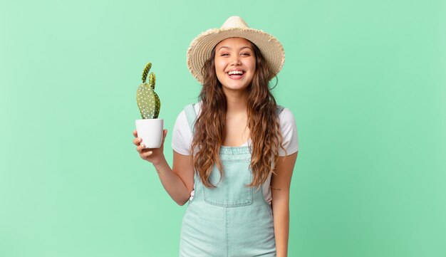 Jovem mulher bonita olhando feliz e agradavelmente surpresa e segurando um cacto