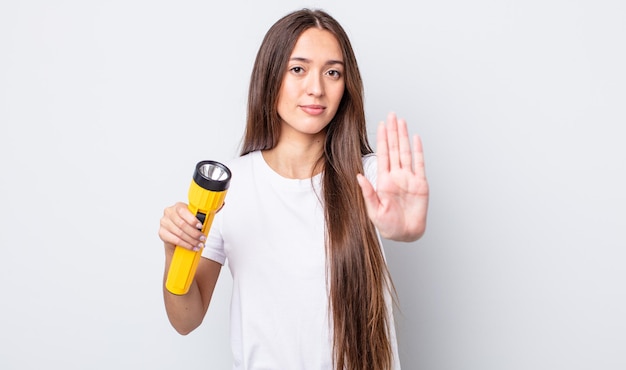 Jovem mulher bonita olhando séria mostrando a palma da mão aberta, fazendo o gesto de parada. conceito de lanterna