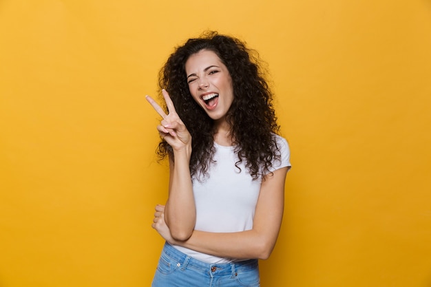 Jovem mulher bonita posando isolada em amarelo, mostrando um gesto de paz.