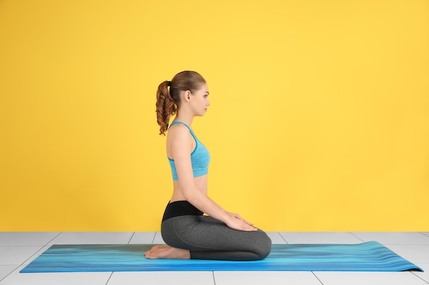 Foto jovem mulher bonita praticando pose de ioga perto da parede colorida dentro de casa