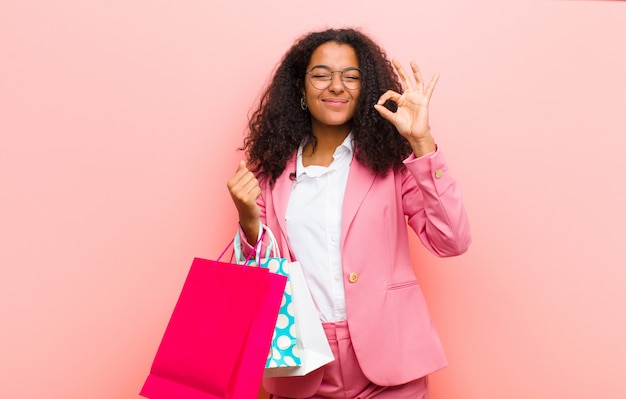 Jovem mulher bonita preta com sacos de compras contra parede rosa