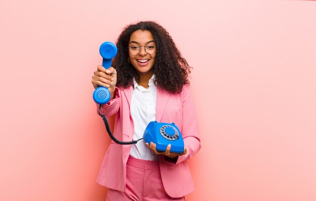 Jovem mulher bonita preta com um telefone vintage contra parede rosa