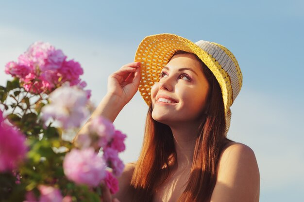 Jovem mulher bonita que levanta perto das rosas em um jardim.