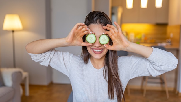 Jovem mulher bonita que recebe a máscara facial do pepino em casa.