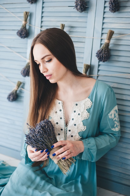 Jovem mulher bonita que senta-se com alfazema contra a parede azul.