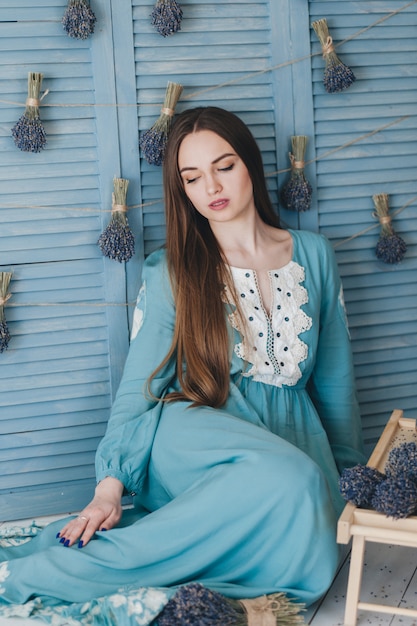 Jovem mulher bonita que senta-se com alfazema contra a parede azul.