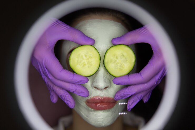 Foto jovem mulher bonita recebendo máscara de argila facial com pepino nos olhos no salão de beleza do spa.