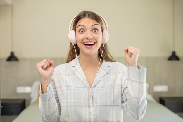 Foto jovem mulher bonita se sentindo chocada, rindo e comemorando o conceito de fones de ouvido de sucesso