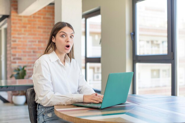 jovem mulher bonita se sentindo extremamente chocada e surpresa trabalhando com um laptop