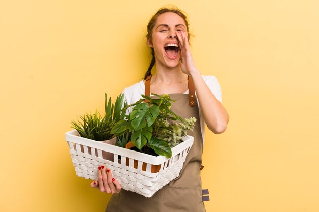 Jovem mulher bonita se sentindo feliz dando um grande grito com as mãos ao lado do conceito de plantas de boca