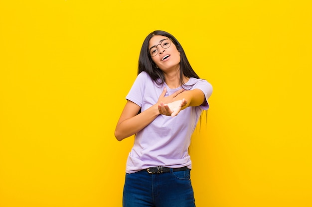 Jovem mulher bonita se sentindo feliz e apaixonada, sorrindo com uma mão ao lado do coração e a outra esticada na frente contra a parede