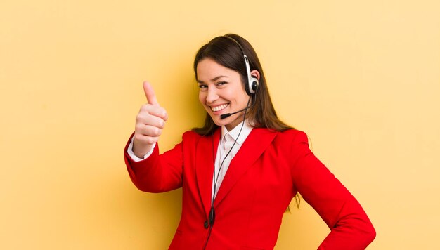 Jovem mulher bonita se sentindo orgulhosa sorrindo positivamente com polegares para cima o conceito de operador de telemarketing