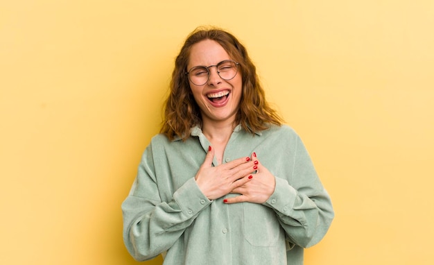 Jovem mulher bonita se sentindo romântica feliz e apaixonada sorrindo alegremente e segurando as mãos perto do coração