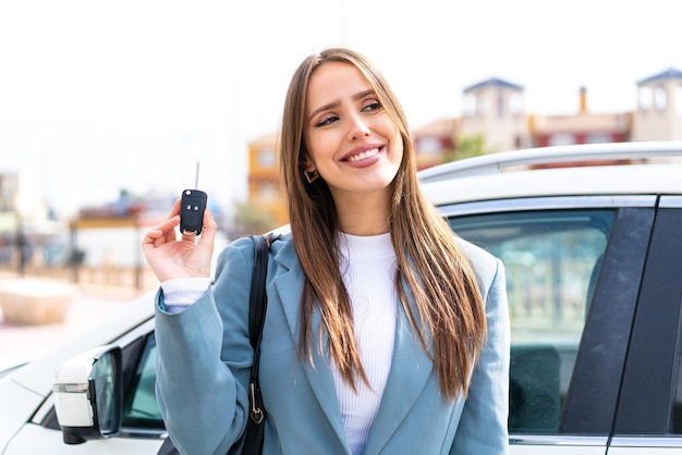 Jovem mulher bonita segurando as chaves do carro ao ar livre olhando para cima enquanto sorri