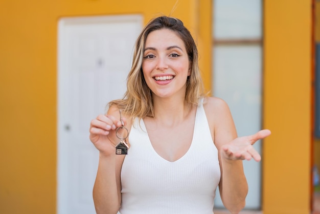 Jovem mulher bonita segurando chaves de casa ao ar livre com expressão facial chocada