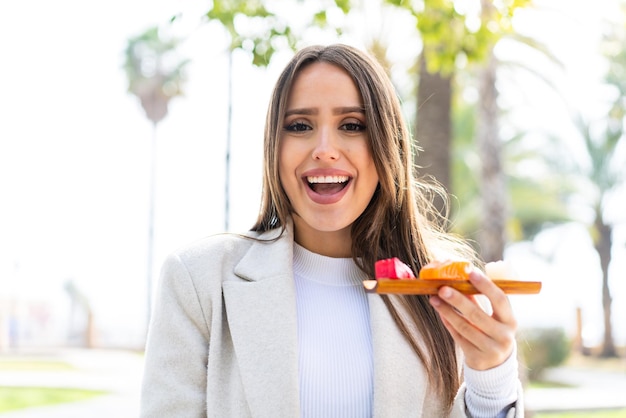 Jovem mulher bonita segurando sashimi ao ar livre com surpresa e expressão facial chocada