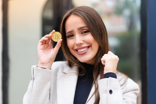 Jovem mulher bonita segurando um Bitcoin ao ar livre