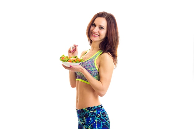 Jovem mulher bonita segurando um garfo e prato branco com salada verde e tomate em fundo branco