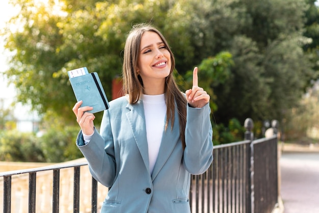 Jovem mulher bonita segurando um passaporte ao ar livre com a intenção de perceber a solução enquanto levanta um dedo