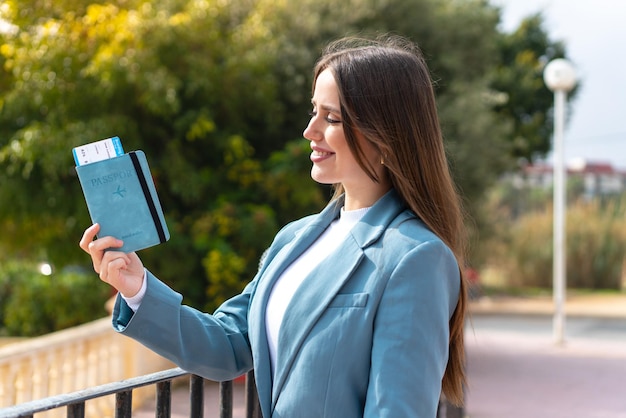 Jovem mulher bonita segurando um passaporte ao ar livre com expressão feliz