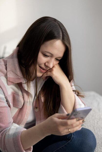 Foto jovem mulher bonita sentada em casa e se comunicando em um smartphone com seu amado e feliz