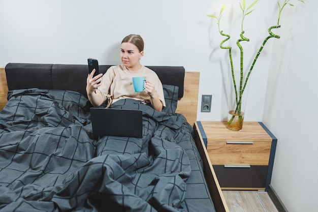 Jovem mulher bonita sentada na cama com café trabalhando com computador em casa trabalho remoto Mulher feliz e sorrindo feliz na cama em casa