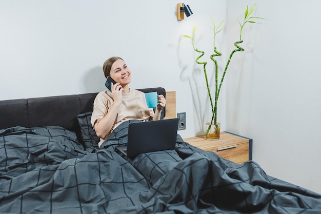 Jovem mulher bonita sentada na cama com café trabalhando com computador em casa trabalho remoto Mulher feliz e sorrindo feliz na cama em casa