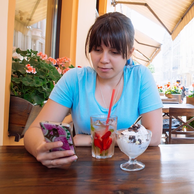 Jovem mulher bonita sentada no café usando seu telefone e bebendo bebidas frescas em dia de verão