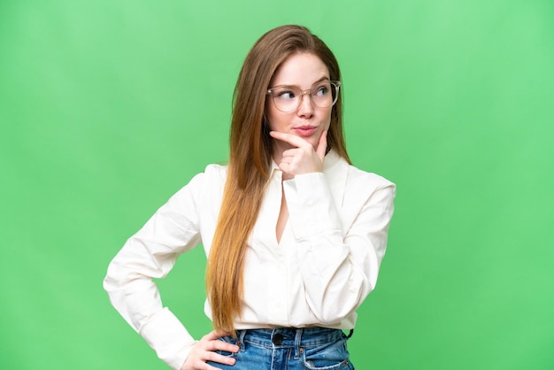 Jovem mulher bonita sobre fundo croma chave isolado, pensando em uma ideia enquanto olha para cima