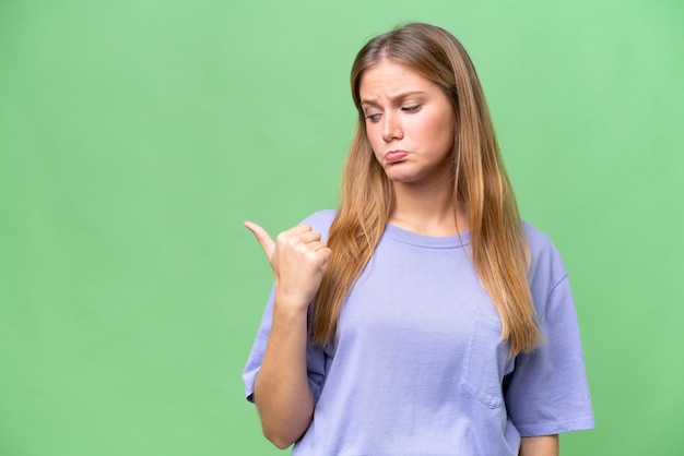 Jovem mulher bonita sobre fundo isolado infeliz e apontando para o lado