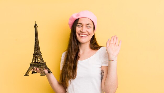 Jovem mulher bonita sorrindo alegremente acenando com a mão dando as boas-vindas e cumprimentando seu conceito de paris