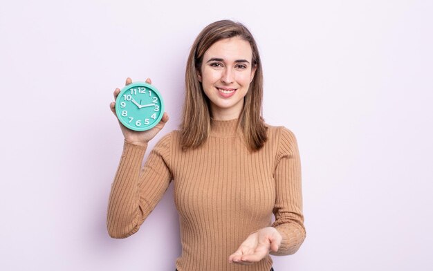 Jovem mulher bonita sorrindo alegremente com amigável e oferecendo e mostrando um conceito. despertador