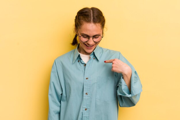 Jovem mulher bonita sorrindo alegremente e casualmente olhando para baixo e apontando para o peito