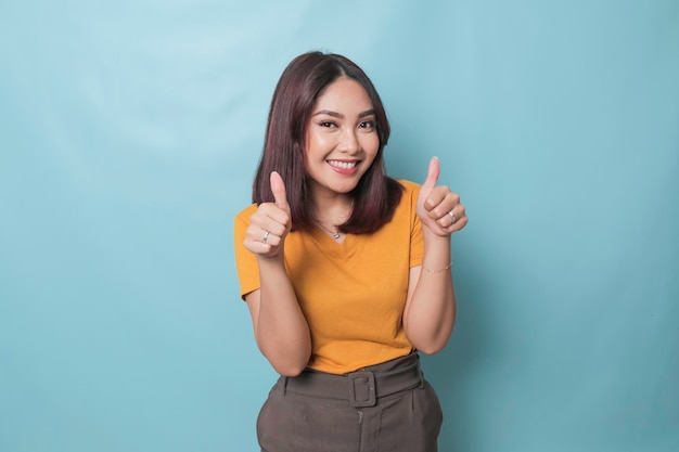 Jovem mulher bonita sorrindo alegremente e parecendo feliz sentindo-se despreocupada e positiva com os dois polegares para cima isolados por fundo azul