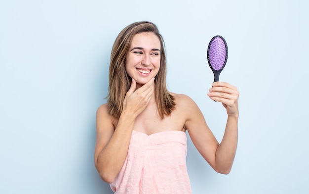 jovem mulher bonita sorrindo com uma expressão feliz e confiante com a mão no queixo. conceito de escova de cabelo