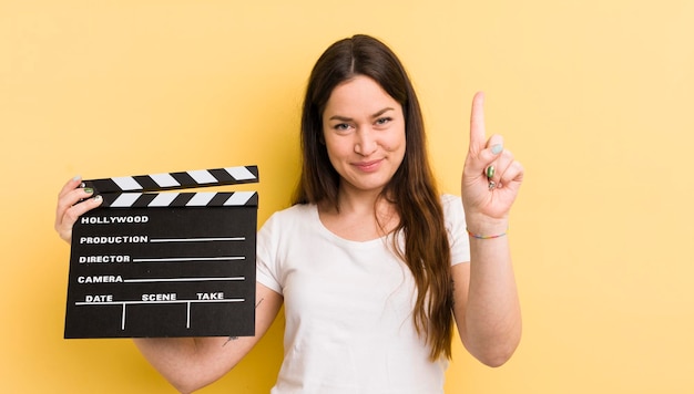 Jovem mulher bonita sorrindo e parecendo amigável mostrando o conceito de badalo de cinema número um