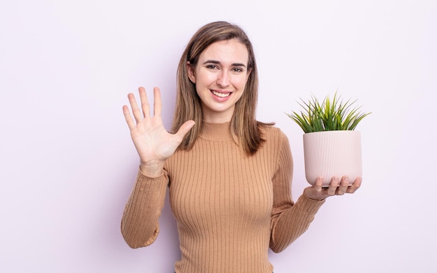 Jovem mulher bonita sorrindo e parecendo amigável mostrando o conceito de planta número cinco