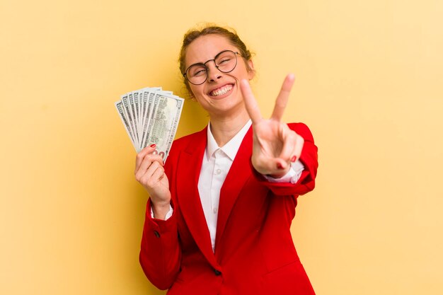 Jovem mulher bonita sorrindo e parecendo feliz gesticulando vitória ou conceito de dinheiro de paz