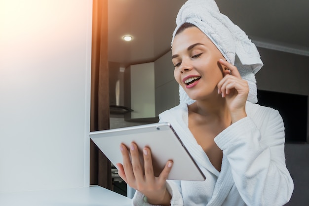 Jovem mulher bonita toalha branca e roupão segurando um tablet