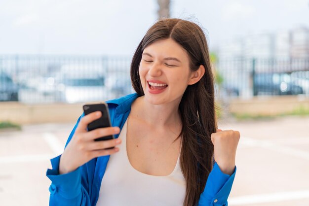 Jovem mulher bonita ucraniana usando telefone celular ao ar livre comemorando uma vitória