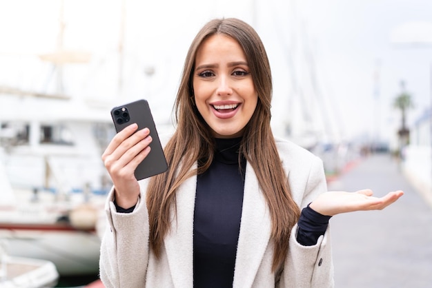 Jovem mulher bonita usando telefone celular ao ar livre com expressão facial chocada