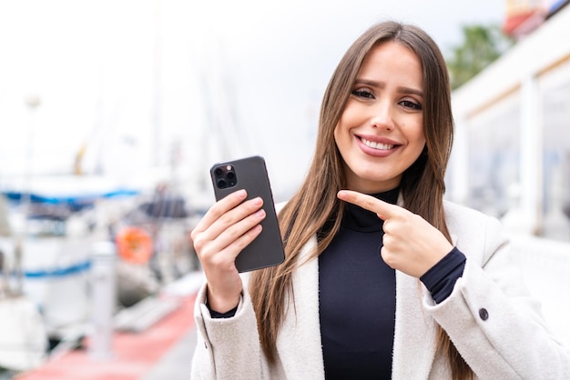 Jovem mulher bonita usando telefone celular ao ar livre com expressão facial de surpresa