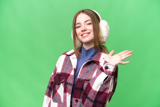 Jovem mulher bonita vestindo regalos de inverno sobre fundo croma chave isolado saudando com a mão com expressão feliz